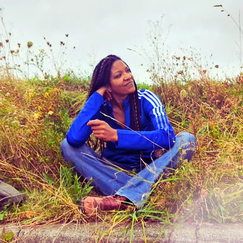 Nelly Sébastien, coach de vie, assise dans la nature, regard posé, illustrant un accompagnement humain sans pression face à la charge mentale.